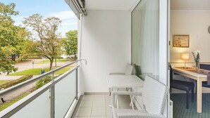 A balcony with a white table and chairs, a view of trees and a road, and a lamp on a table inside. - Cozy and quiet vacation apartment in the center of Bad Füssing (Bad Füssing)