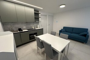 Cozinha moderna com armários cinza, mesa de jantar branca e sofá azul.