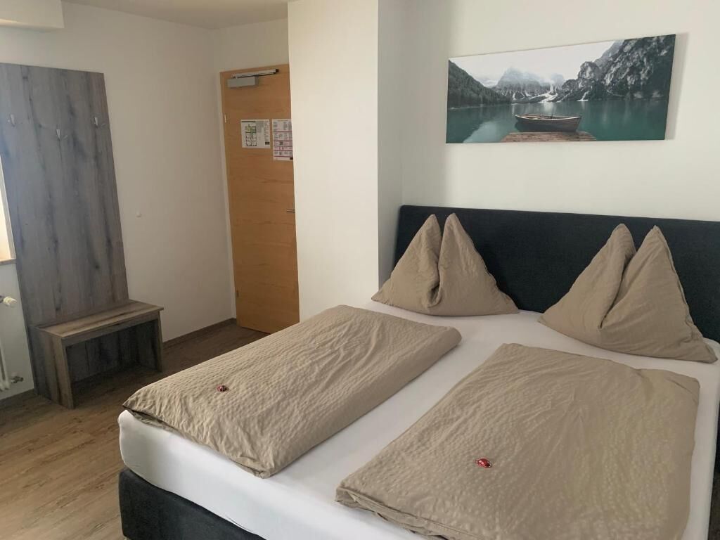 A bedroom with a bed, pillows, a wooden bench, a door, and a wall-mounted picture.