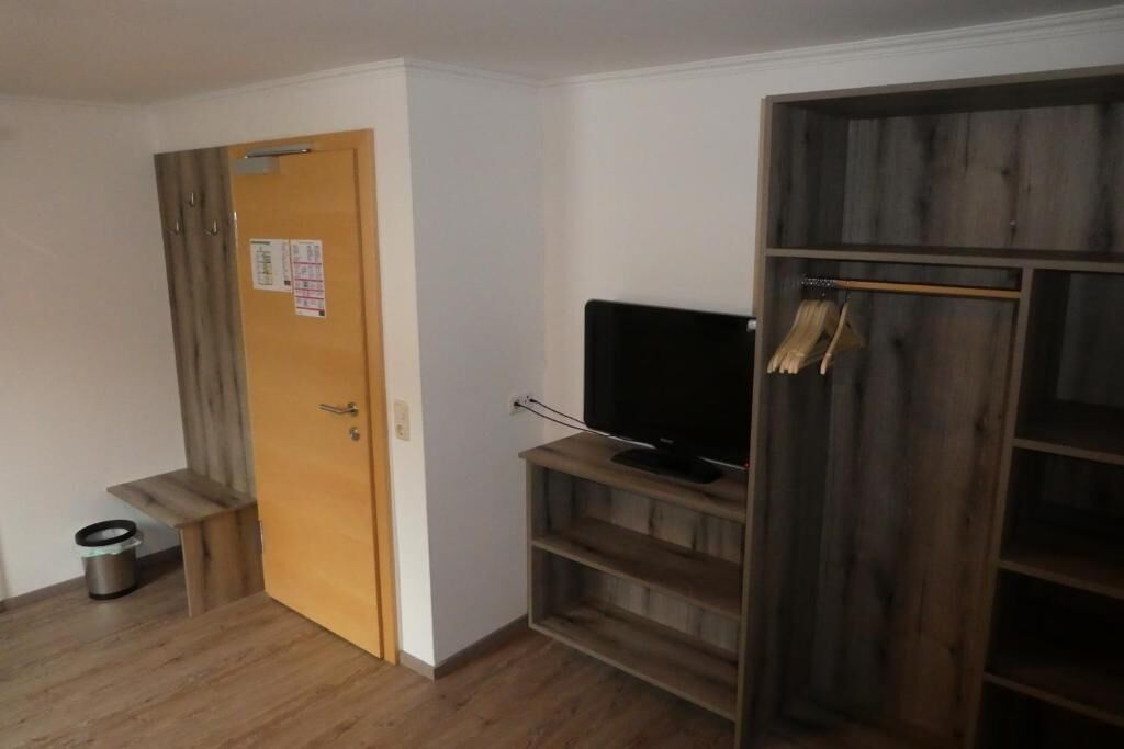 A room with a wooden door, a television on a wooden stand, and a wooden wardrobe.