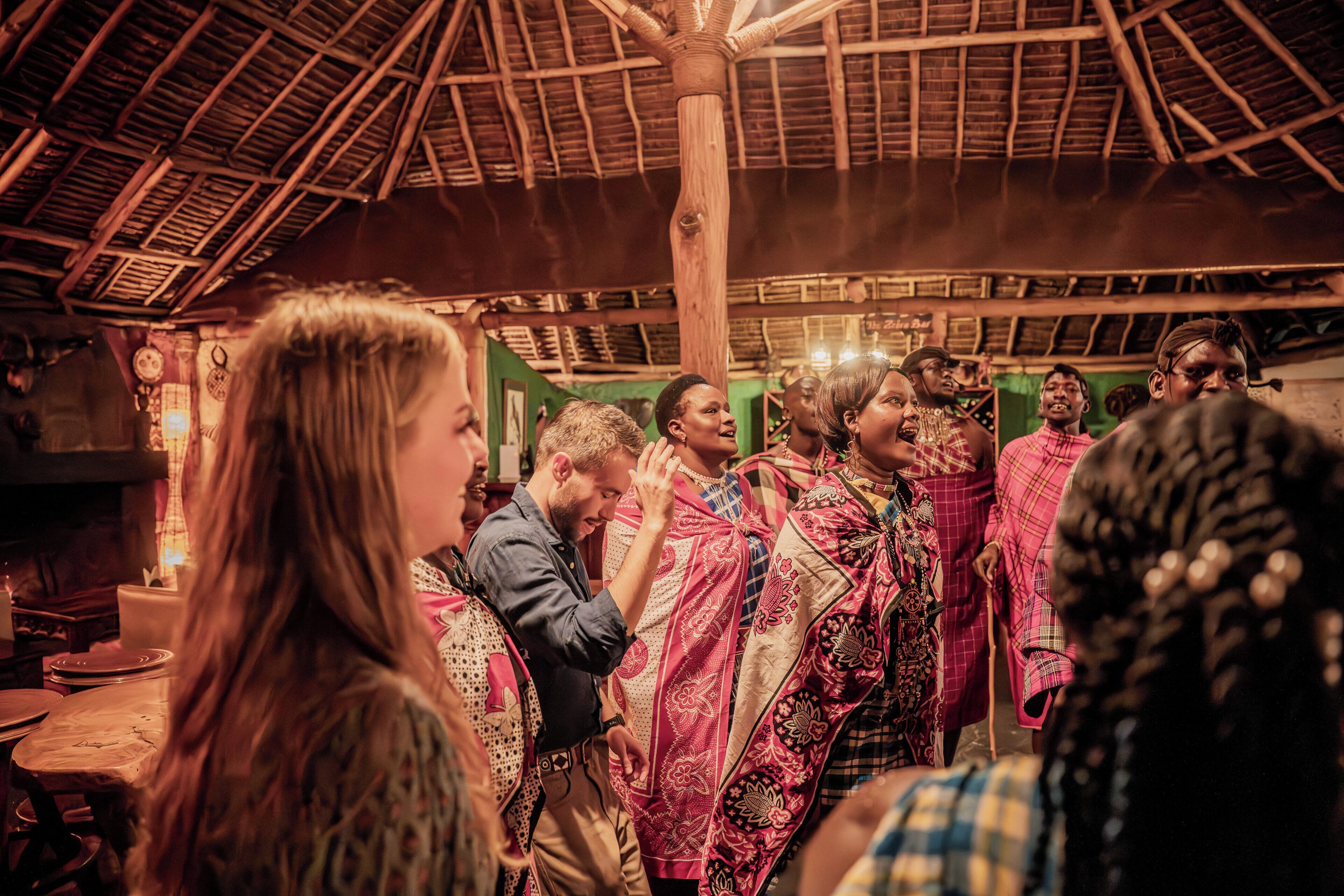 A group of people in a rustic, wooden interior with a thatched roof, traditional decor, and a bar area.