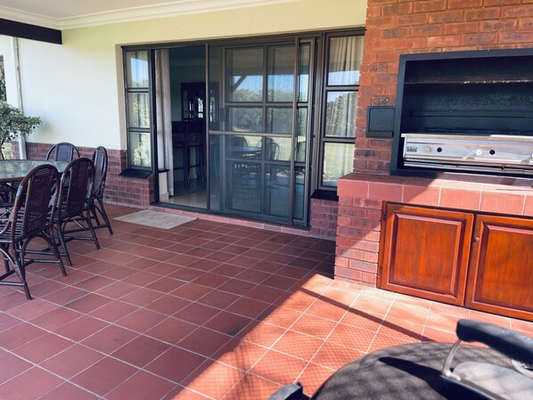 A patio with a grill, chairs, and a sliding glass door leading to an indoor area.