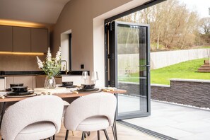 A modern kitchen with a dining area, large glass doors, and a view of the outdoors. - Megan's Hideaway Luxury 4 Bed Retreat (Stourport-on-Severn)