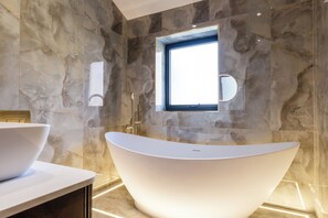 A modern bathroom with a freestanding bathtub, marble walls, and a window providing natural light. - Megan's Hideaway Luxury 4 Bed Retreat (Stourport-on-Severn)
