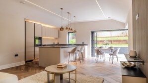 A modern kitchen with a central island, dining area with chairs, and a view of the outdoors. - Megan's Hideaway Luxury 4 Bed Retreat (Stourport-on-Severn)