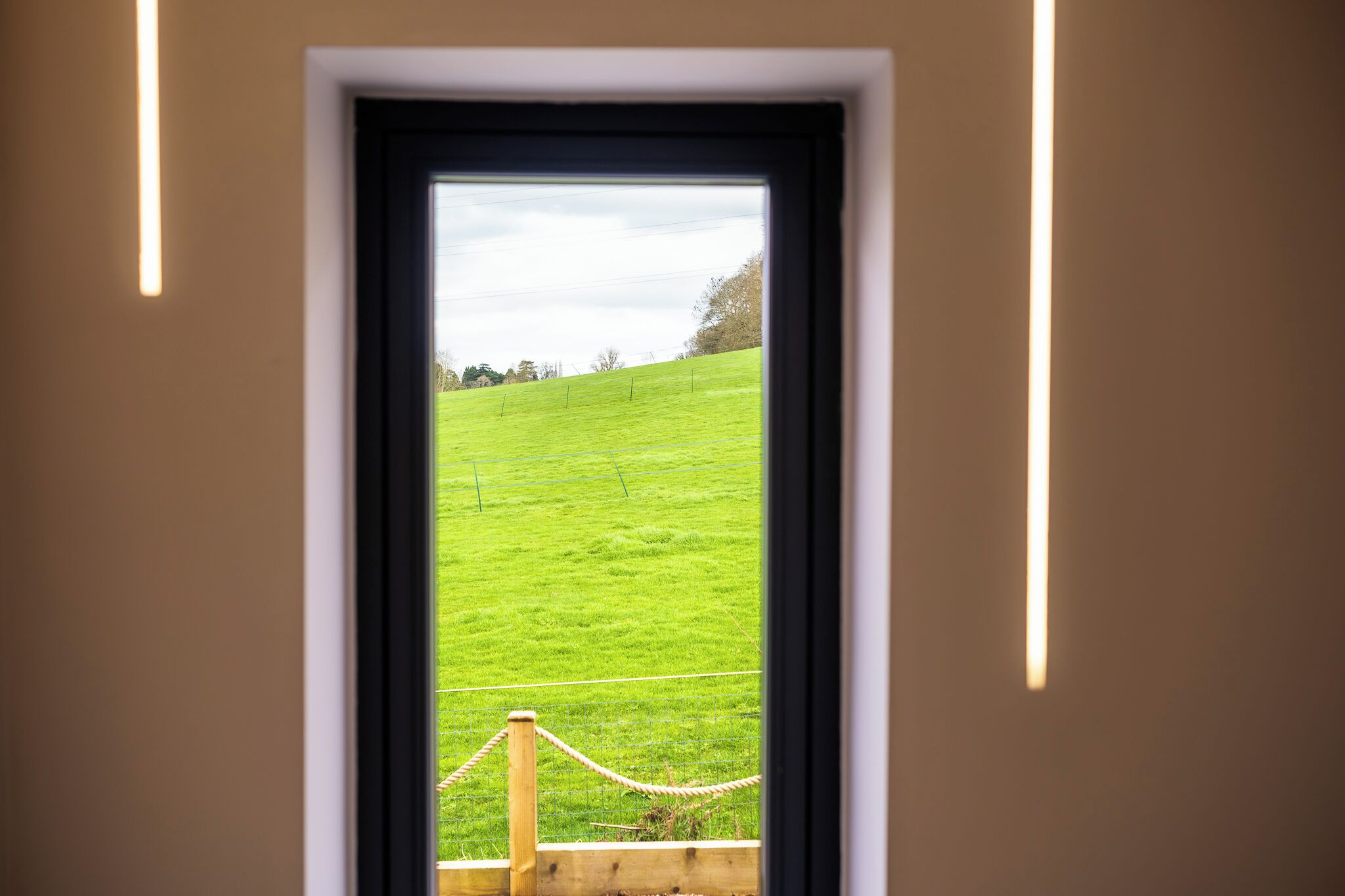 A window with a view of a green field and a wooden fence.
