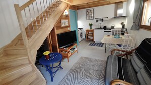 Un escalier en bois mène à un espace de vie comprenant un téléviseur, un canapé et une table à manger.
