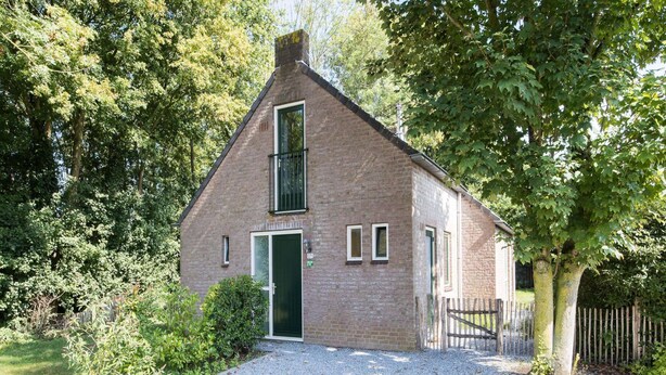 A small brick house with a gravel driveway, a wooden gate, and a tree in front. - Woodland Bungalow Retreat for 4 (Ewijk)