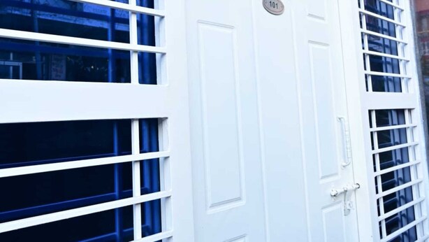 Una puerta blanca con una placa de identificación, flanqueada por persianas verticales.