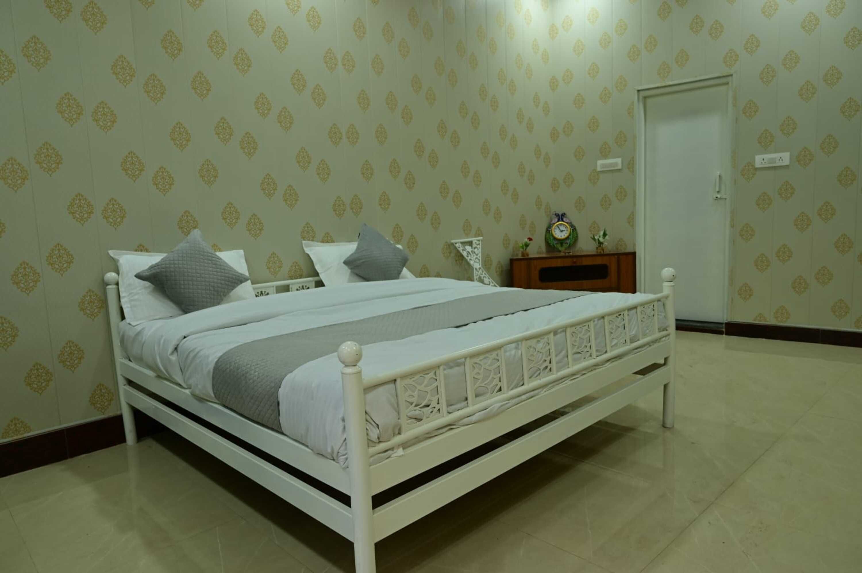 A neatly made bed with white bedding, a small bedside table with a clock, and a door in the background.