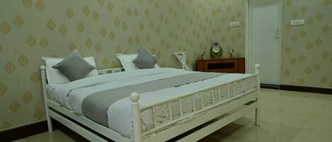 A neatly made bed with white bedding, a small bedside table with a clock, and a door in the background.