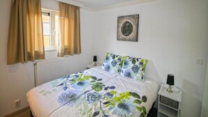 A bedroom with a bed, curtains, a radiator, a wall-mounted lamp, a small bedside table, and a picture on the wall. - Chalet With 3 Bedrooms and Infrared Sauna (West-Graftdijk)