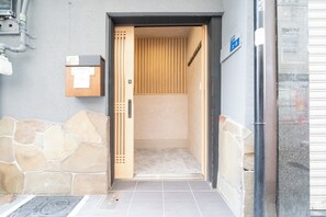 An entrance to a building with a stone wall, a wooden door, and a tiled floor. - 1 min. from Namba station｜90 sq.m. of space｜Newly opened｜Two toilets and showers provided｜Comfortable stay (2-2-8 Dotonbori, Chuo-ku)