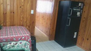 A room with wooden walls, a black refrigerator, a table with a checkered tablecloth, and a tiled floor.