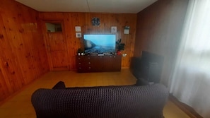 A living room with wooden walls, a television, a sofa, and a small table with items on it.