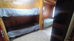 A room with wooden walls, a bunk bed, a small table, and a door leading to another room.