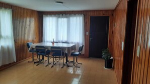 A room with a wooden paneled wall, a large table with chairs, a door, and a potted plant.
