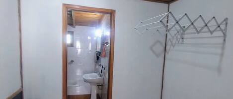 A room with a wooden ceiling, a tiled floor, a doorway leading to a bathroom, and a clothes drying rack on the wall.