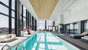 An indoor swimming pool with clear glass walls, a bamboo ceiling, and a view of the cityscape. - Moxy Ottawa Downtown (OTTAWA)