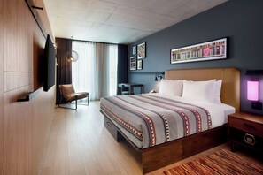 A modern hotel room with a large bed, a desk, a chair, and a television. - Moxy Ottawa Downtown (OTTAWA)