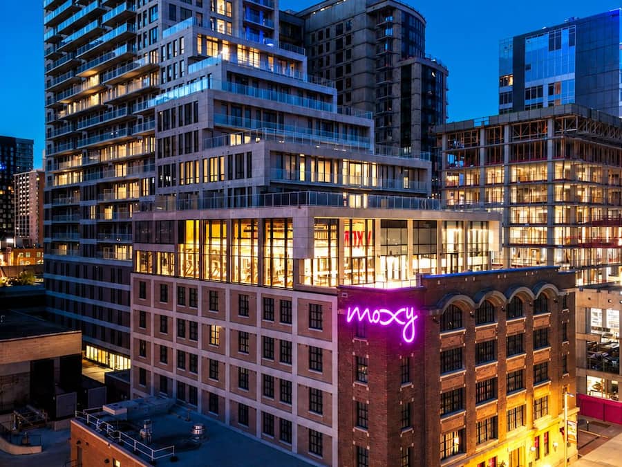 A multi-story hotel with a prominent neon sign, large windows, and a rooftop area.