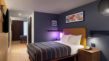 Une chambre d’hôtel moderne, équipée d’un lit, d’une table de chevet, d’une lampe et d’une œuvre d’art au mur.