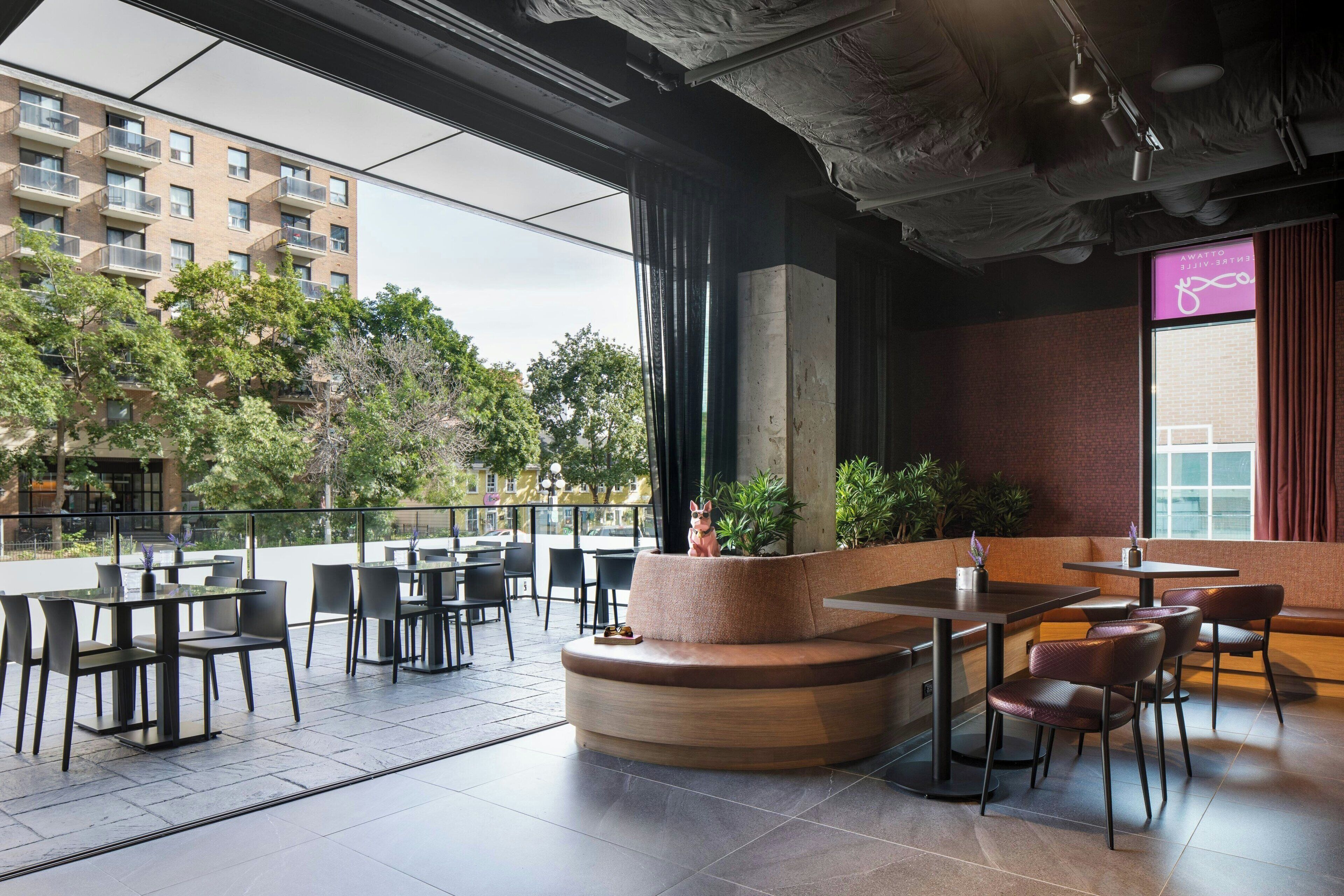 An outdoor seating area with tables and chairs, a wooden planter, and a view of a building with balconies.