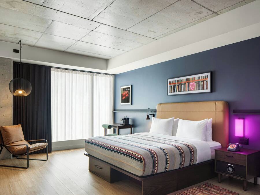 A modern bedroom with a large bed, a chair, a bedside table, a lamp, and a bookshelf.