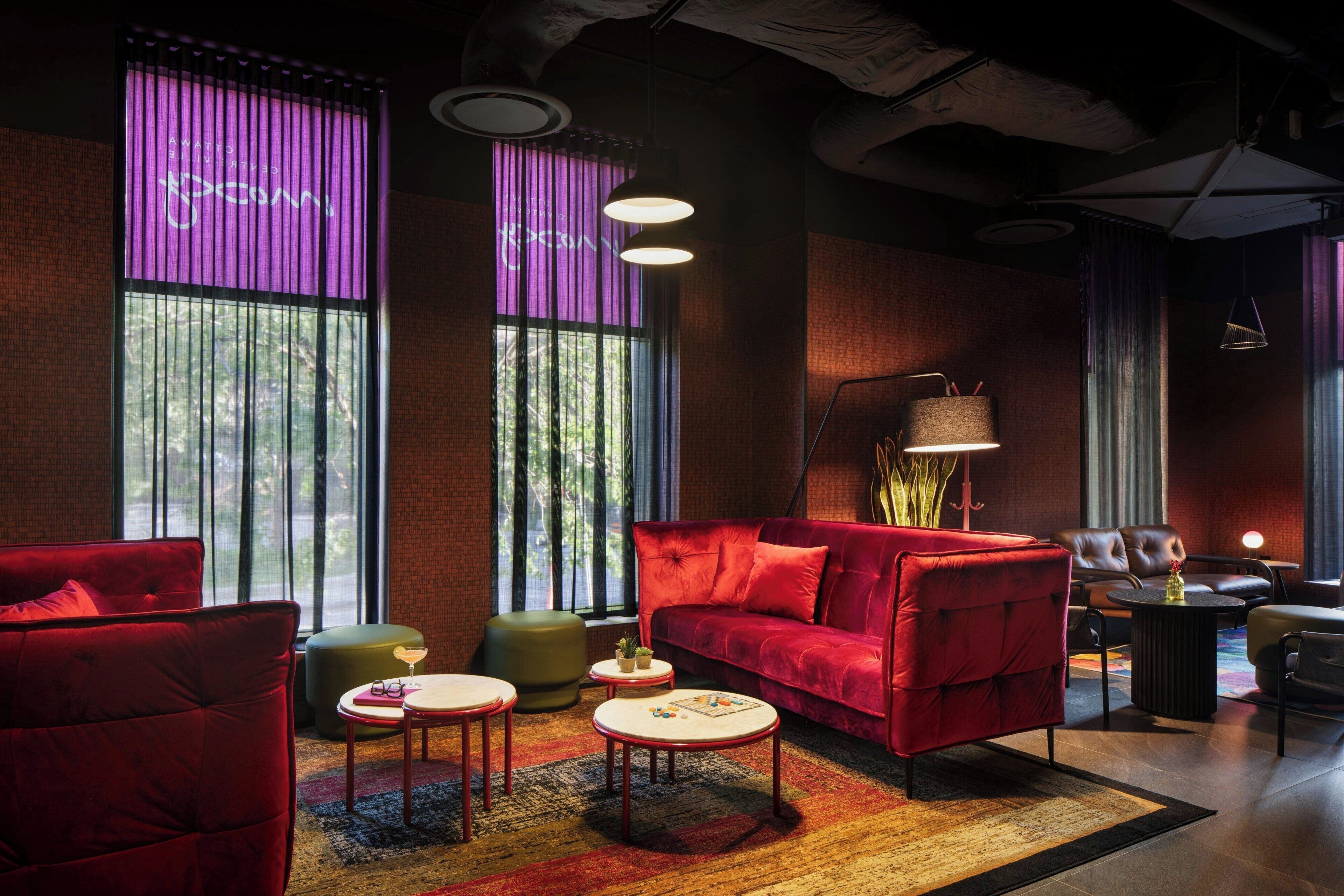 A modern lounge area with a red sofa, multiple seating options, and a large window providing natural light.