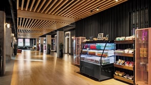 A modern interior with a wooden slatted ceiling, a refrigerated display case with beverages, and a snack bar. - Moxy Ottawa Downtown (OTTAWA)
