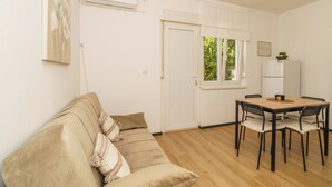 A room with a beige sofa, a wooden dining table with chairs, a white door, and a window with a view of greenery. - Stylish vacation apartment in Dramalj - beach just 250 m away (Dramalj)