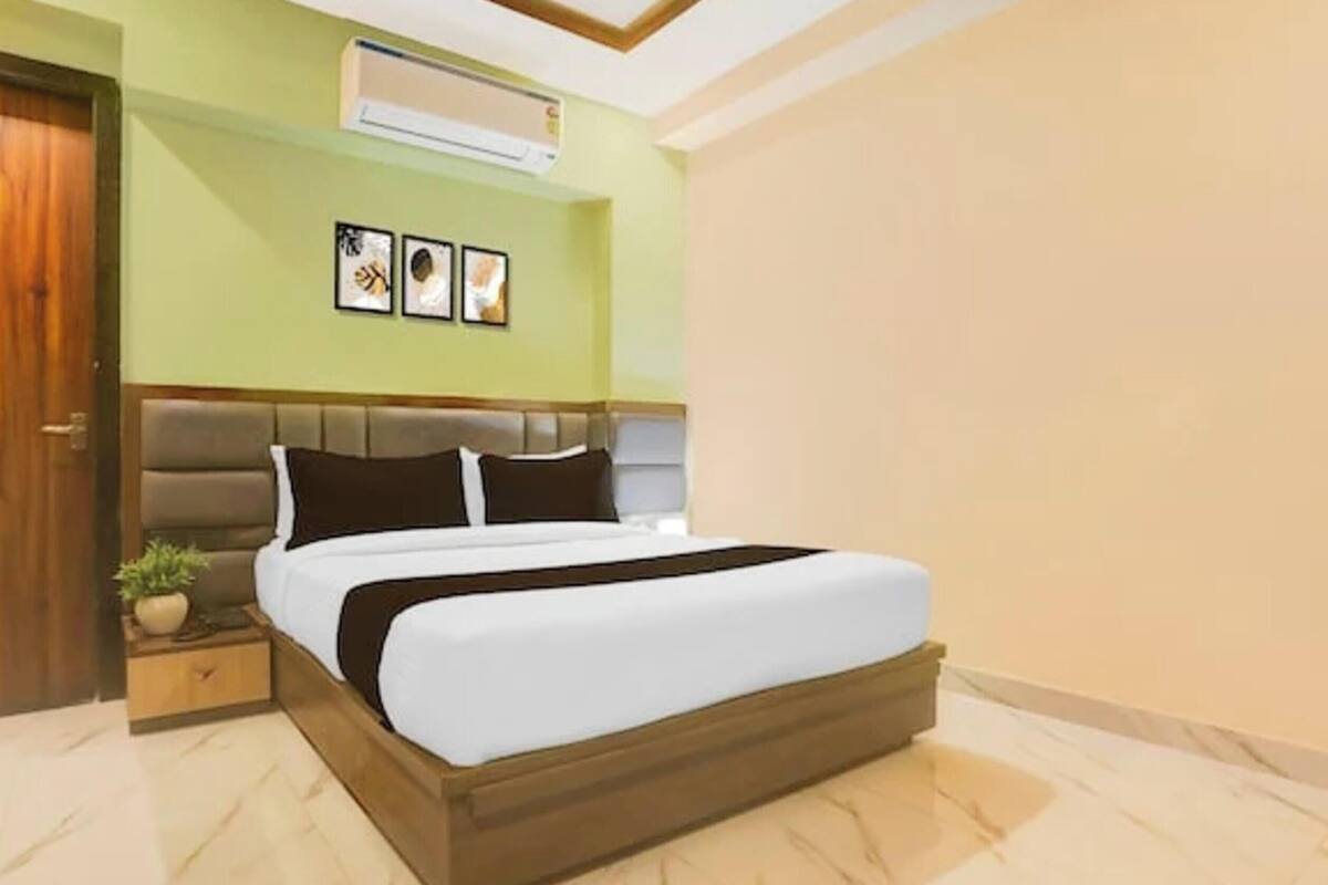 Un dormitorio con una cama, una mesita de noche, una planta en maceta y un aire acondicionado instalado en la pared.