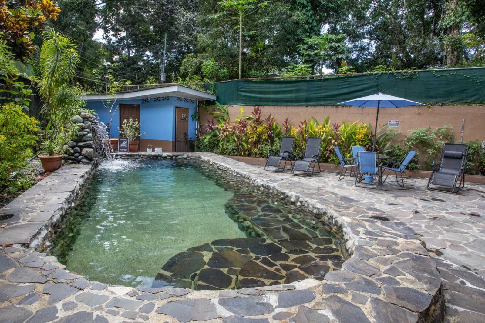 Une piscine en pierre, dotée de chaises longues et bordée d’un petit bâtiment surmonté d’un toit bleu.