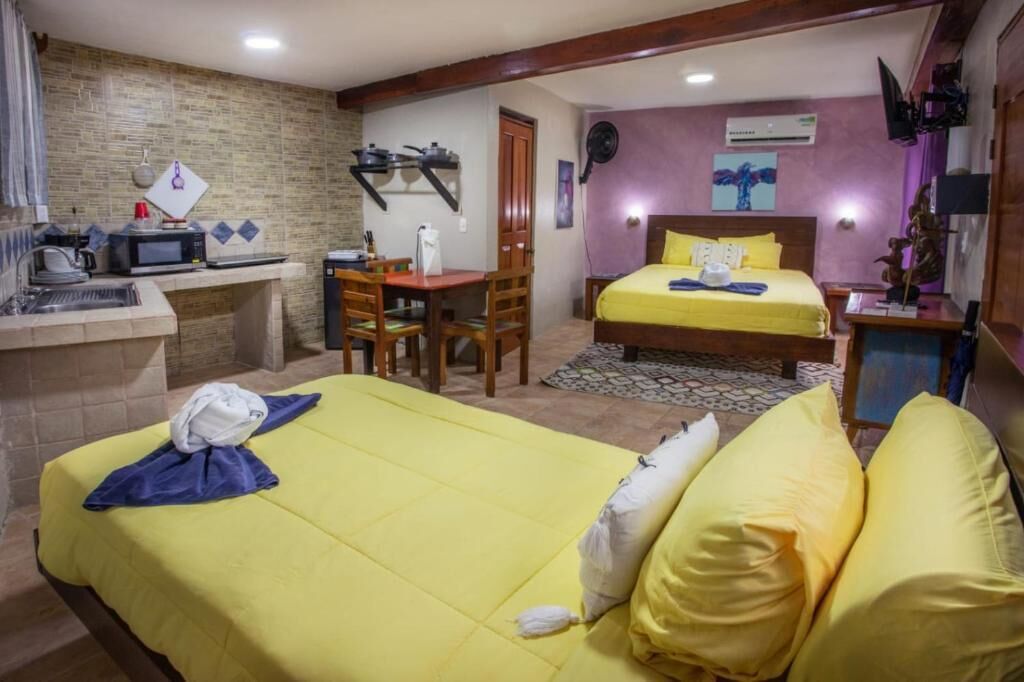 A hotel room with a bed, a desk with a microwave, a chair, a small table, and a fan.