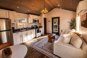 Eine moderne Küche mit Edelstahlgeräten, ein Essbereich mit rundem Tisch und ein Wohnzimmer mit Sofa und einem gemusterten Teppich.