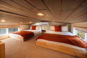 Interior de una cabaña con dos camas de madera, una ventana y un techo con vigas de madera.