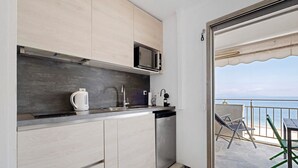 Une cuisine compacte équipée d’un four à micro-ondes, d’une bouilloire et d’un lave-vaisselle, donnant sur un balcon avec vue sur la mer.
