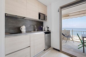 Cocina compacta con microondas, hervidor y lavavajillas, que da a un balcón con vistas al mar.