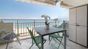 Un balcon avec une table et des chaises, une plante en pot et une vue sur la mer.