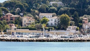 Un port de plaisance avec des bateaux, une digue rocheuse et des bâtiments dotés de balcons donnant sur l’eau.