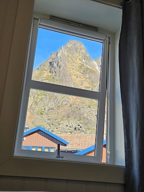 A window with a view of a mountain and a building with a red roof.