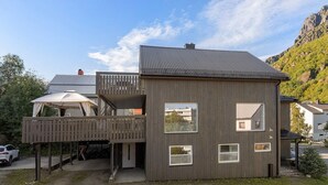 A two-story building with a balcony, a garage, and a small outdoor seating area. - Apartment close to the mountain - free parking (Nordland)