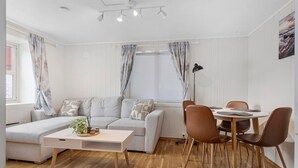 A modern living room with a sofa, a dining table with chairs, a coffee table, and a window with curtains. - Apartment close to the mountain - free parking (Nordland)