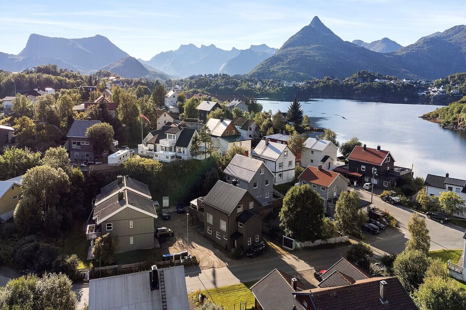 A residential area with houses, a road, and a lake with mountains in the background.
