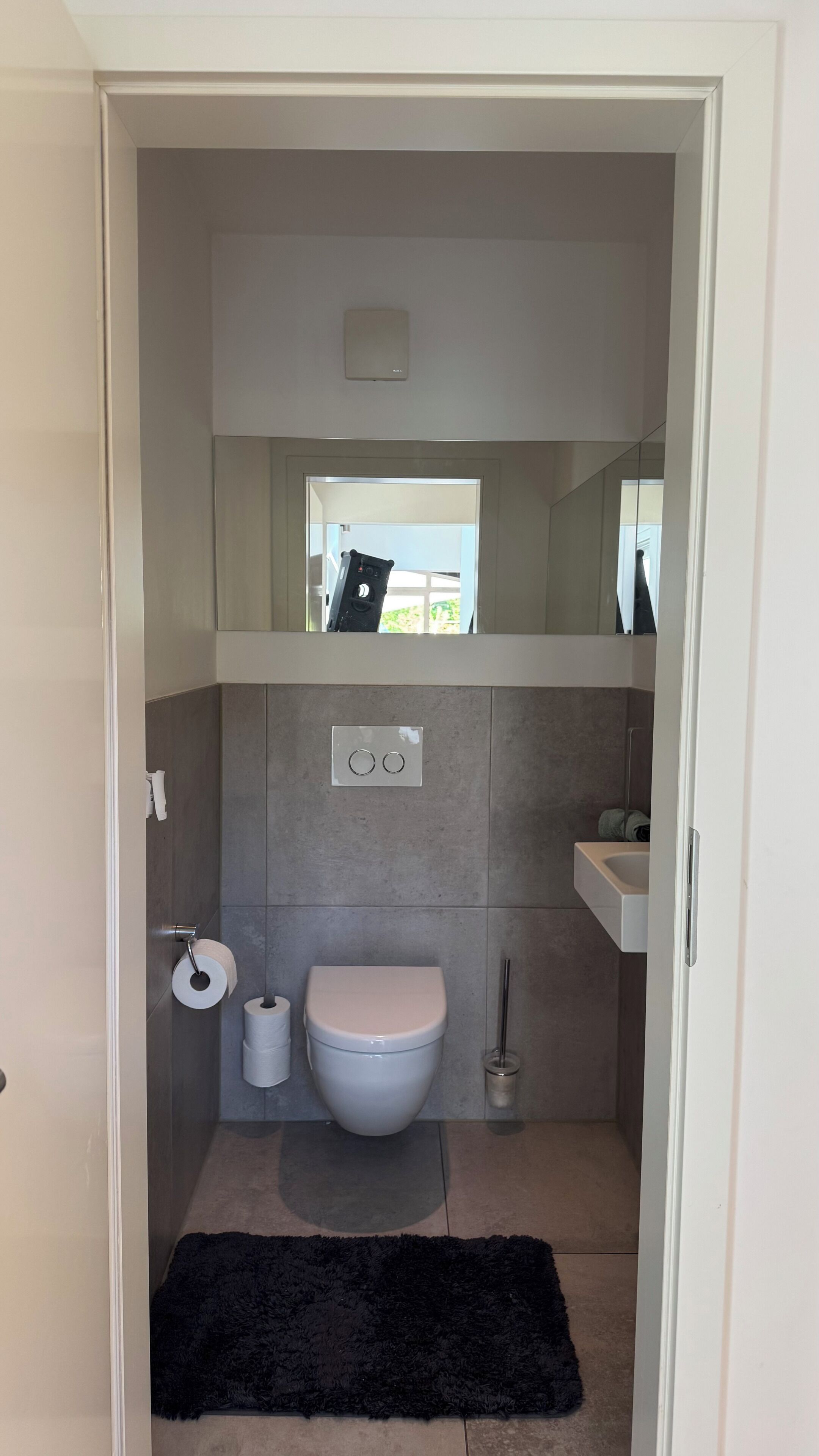 Ein kleines Badezimmer mit Toilette, zwei Toilettenpapierrollen, einem schwarzen Teppich und einem kleinen Fenster.