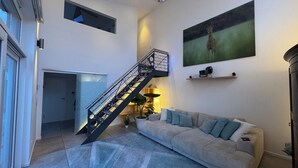A modern living room with a staircase, a sofa, a painting, and a small shelf.