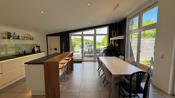 A modern kitchen with a central island, a dining area with a long table, and large sliding glass doors leading to an outdoor patio.