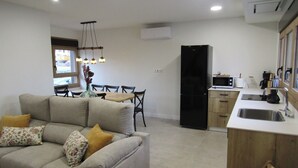 Una sala de estar con un sofá, una mesa de comedor con sillas, y un área de cocina con refrigerador, microondas y lavaplatos.