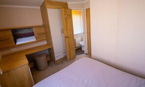 Un dormitorio pequeño con cama, armario de madera y una pequeña estantería.