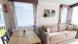 Ein gemütliches Wohnzimmer mit Holztisch, beiger Couch und einer Wandregal mit Pflanzen.
